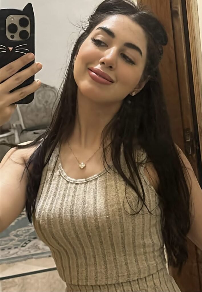 A woman in jeans and a stylish top poses confidently for a photo, smiling at the camera.